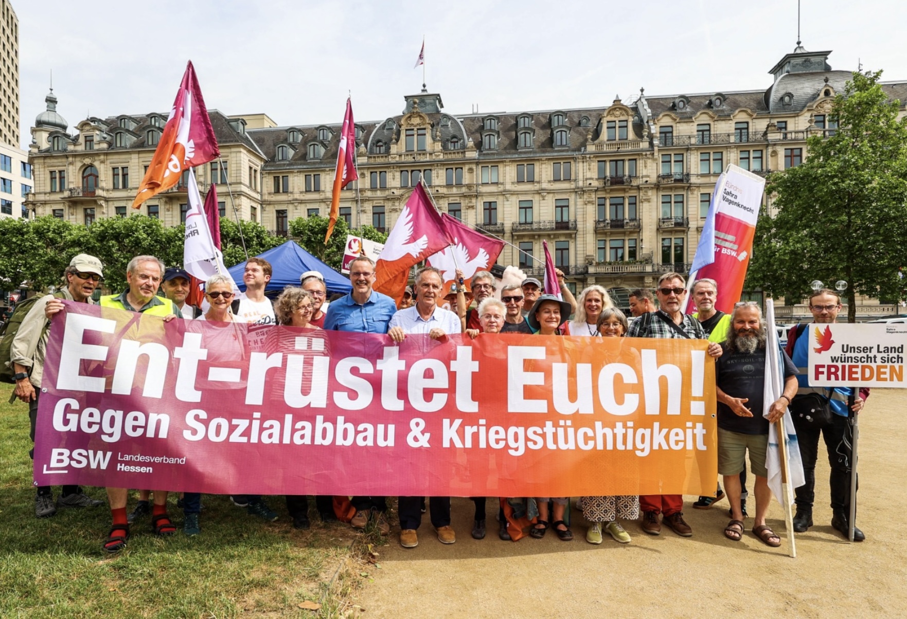 Menschen auf einer Demo mit Transpi und Flaggen. Auf dem Tranpi steht Ent-rüstet Euch! Gegen Sozialabnau und Kriegstüchtigkeit."